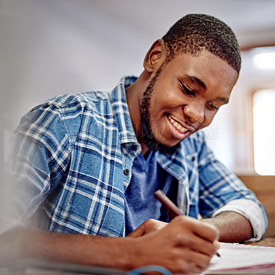 Buy stock photo Shot of a smiling young man writing in notebook while sitting at a table in an office