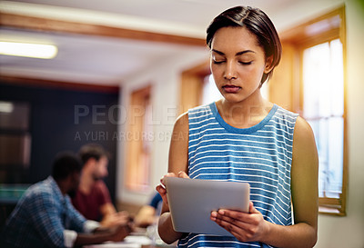 Buy stock photo Shot of a young woman standing in an office using a digital tablet with colleagues in the background
