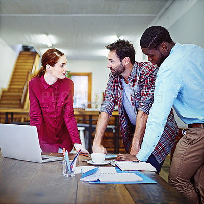 Buy stock photo Shot of a group of colleagues talking together while leaning on a table in an office