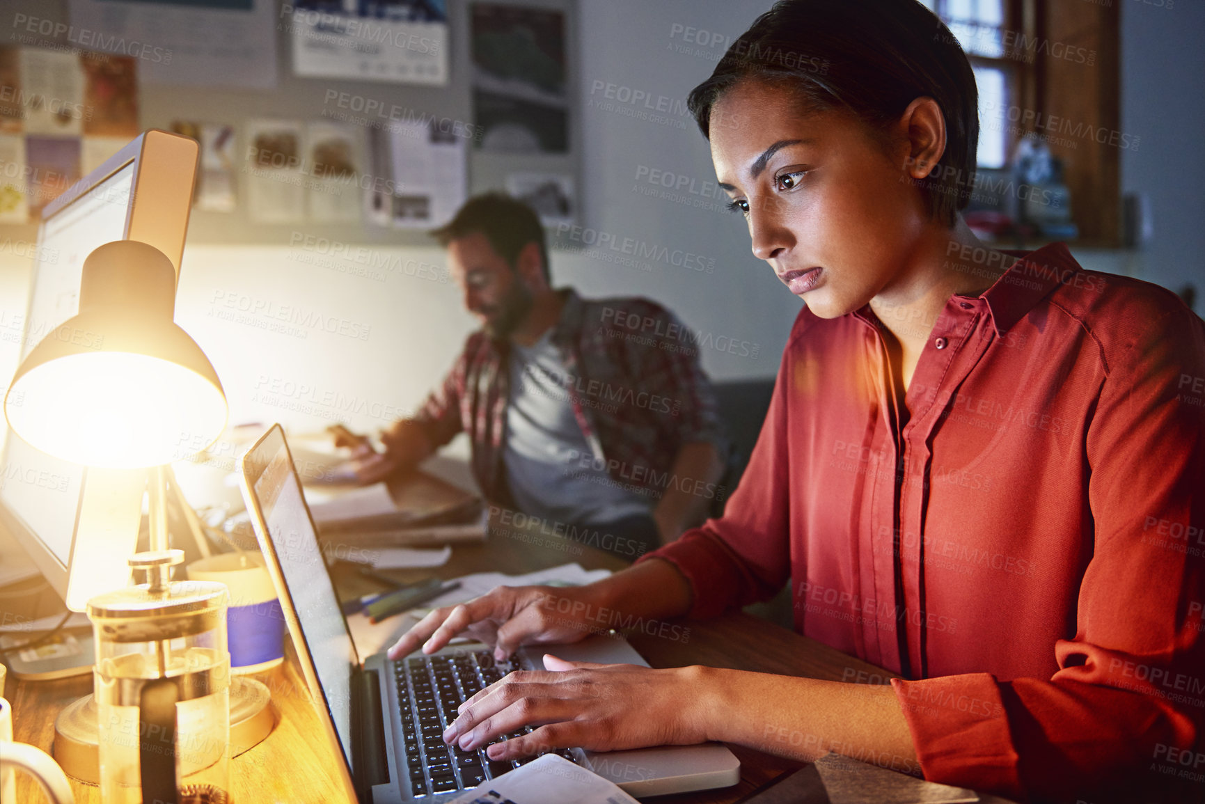 Buy stock photo Shot of a young woman working on a laptop in an office in the evening
