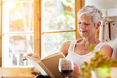 Buy stock photo Shot of a mature woman relaxing on her sofa at home reading a book