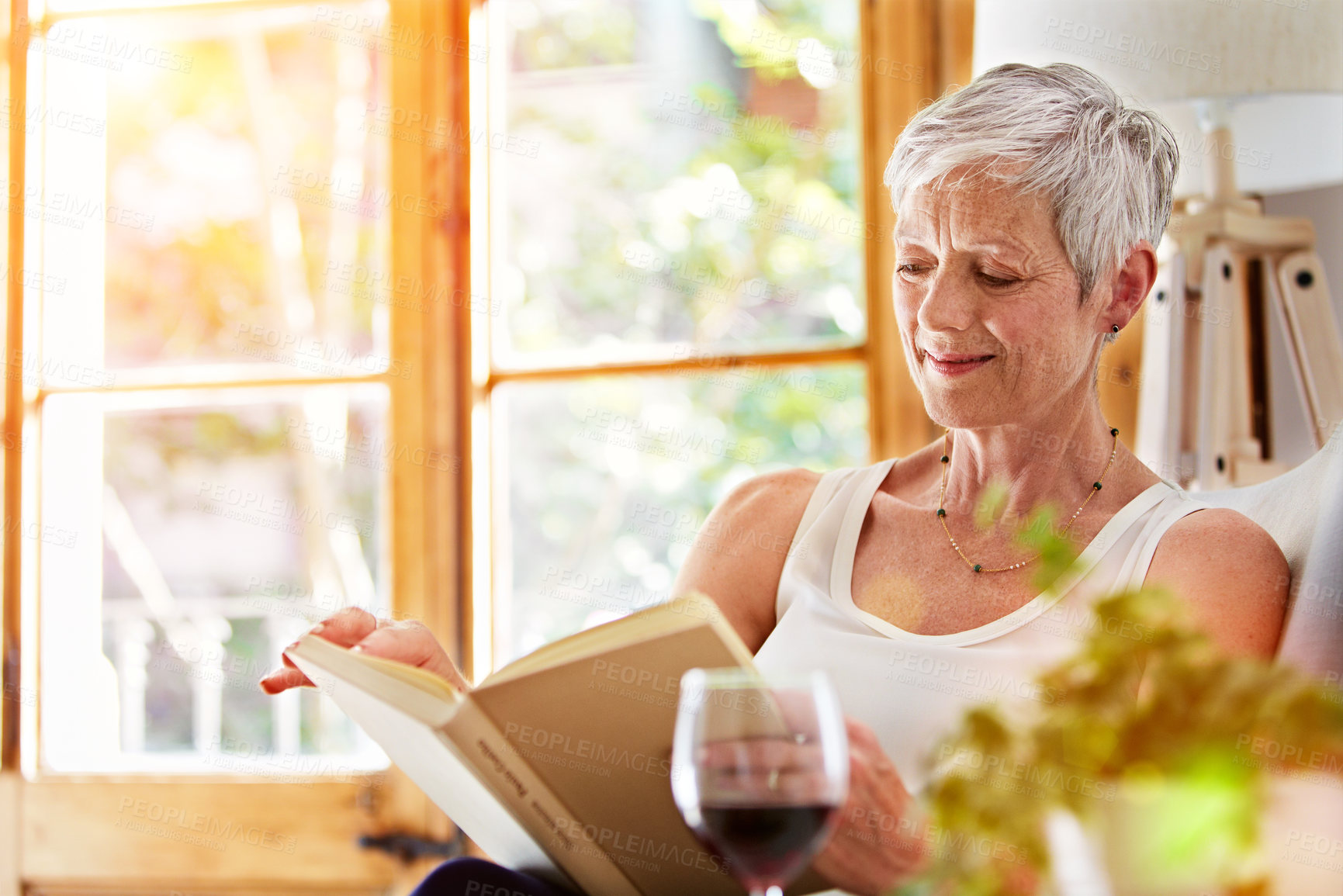 Buy stock photo Shot of a mature woman relaxing on her sofa at home reading a book