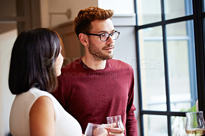 Buy stock photo Shot of a group of friends drinking wine and talking together in a kitchen at a get-together