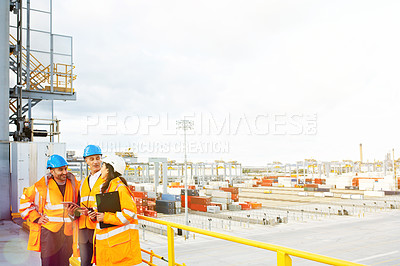 Buy stock photo Shot of three coworkers in protective workwear talking together while standing on a large commercial dock