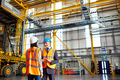 Buy stock photo Shot of two warehouse workers talking together inside of a large warehouse