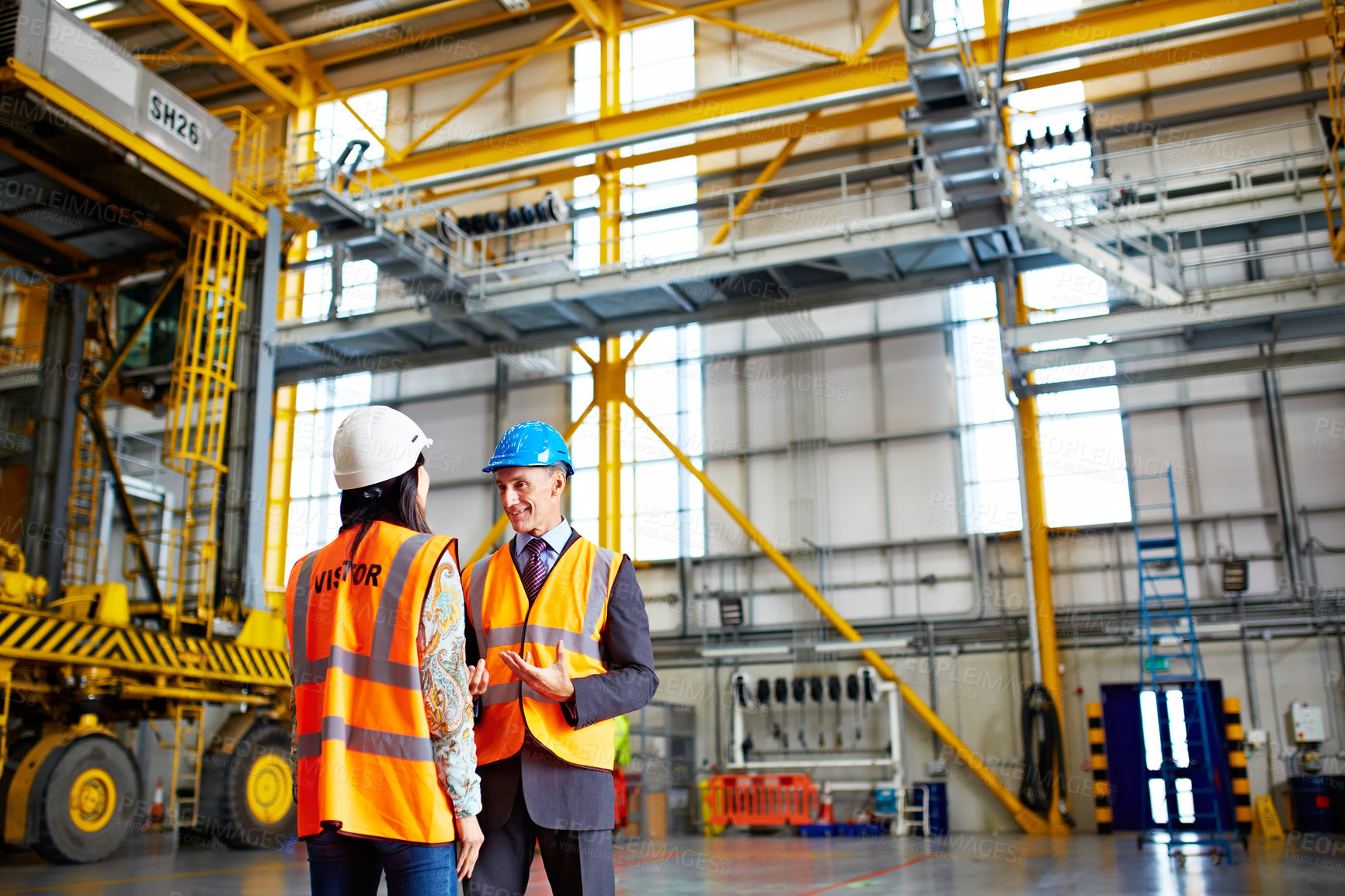 Buy stock photo Shot of two warehouse workers talking together inside of a large warehouse