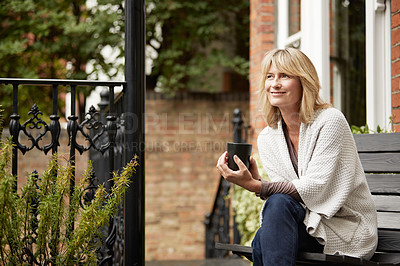 Buy stock photo Shot of a mature woman sitting on a bench on her front porch drinking a coffee