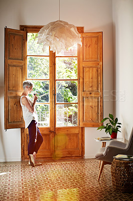 Buy stock photo Shot of a mature woman standing by a window at home drinking a glass of wine