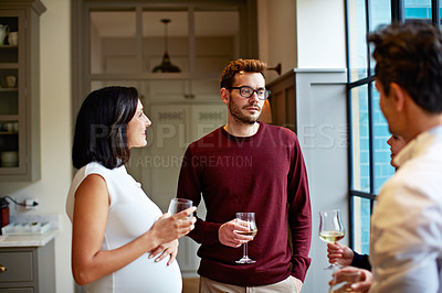 Buy stock photo Shot of a group of friends drinking wine and talking together in a kitchen at a get-together