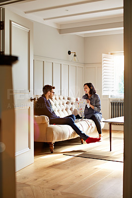 Buy stock photo Shot of a young pregnant woman showing her husband baby clothing while sitting on their sofa