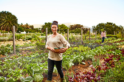 Buy stock photo Portrait of a smiling woman standing in her organic garden with her husband working in the background