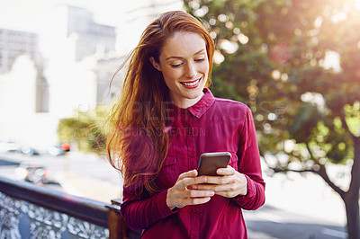 Buy stock photo Shot of a young woman sending a text message while standing outside