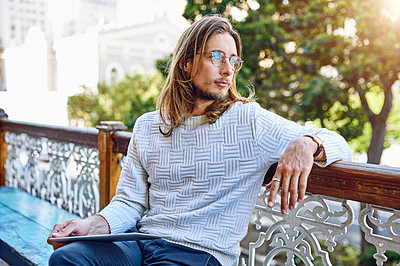 Buy stock photo Shot of a young designer sitting on a bench outside of his office using a digital tablet