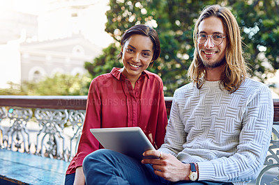 Buy stock photo Portrait of two young designers sitting together on a bench outside of their office using a digital tablet