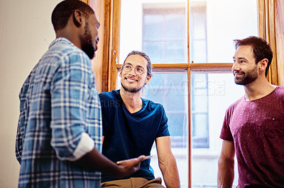 Buy stock photo Shot of three male colleagues talking together while standing in an office