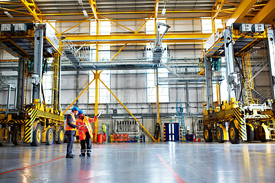 Buy stock photo Shot of two warehouse workers talking together over a clipboard inside of a large warehouse