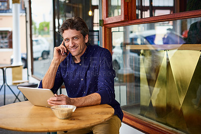 Buy stock photo Shot of a mature man sitting on patio table at a cafe using a tablet and cellphone