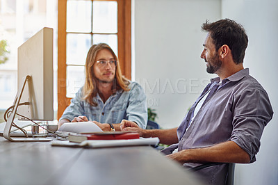 Buy stock photo Shot of two colleagues talking together while working on a computer at a desk in an office