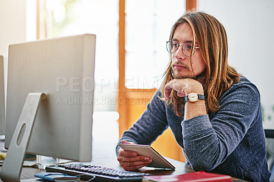 Buy stock photo Shot of a focused young man sitting at his desk in an office working on a computer
