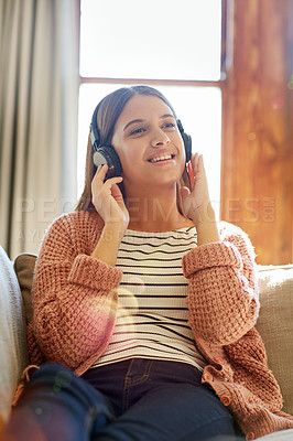 Buy stock photo Shot of a smiling young woman sitting on her sofa listening to music on headphones
