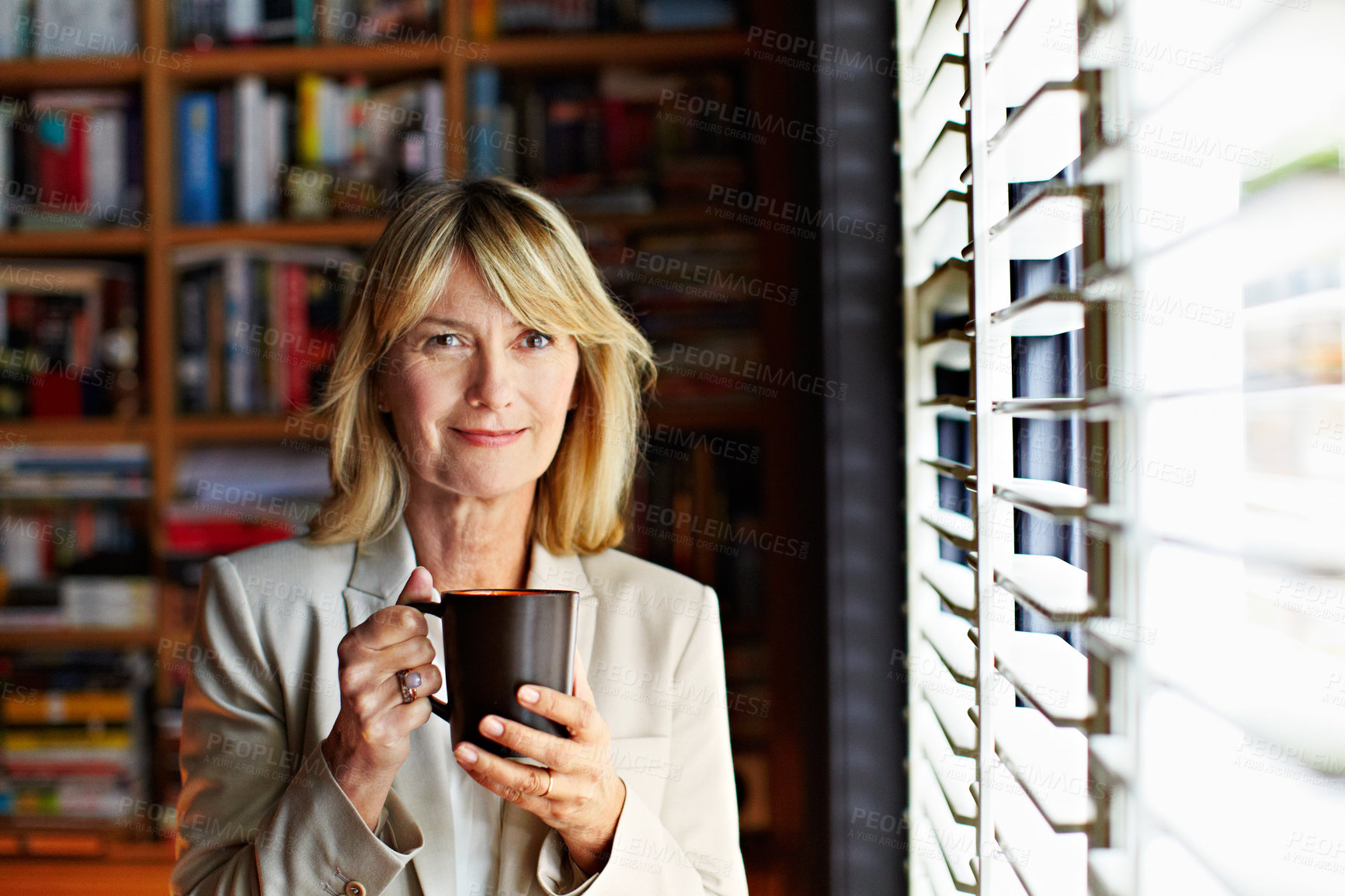 Buy stock photo Portrait of a mature businesswoman drinking coffee while standing at a window in her home