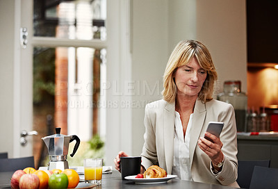 Buy stock photo Shot of a mature businesswoman using her phone while eating breakfast at home