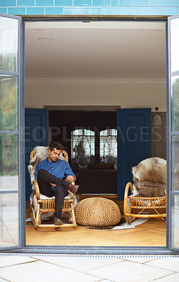 Buy stock photo Shot of a young man using a digital tablet while relaxing on a rocking chair at home