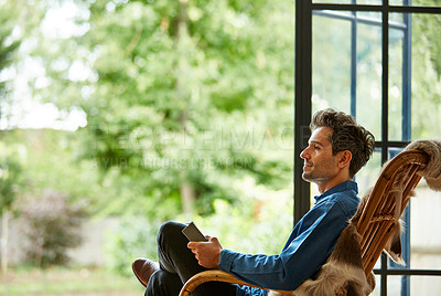 Buy stock photo Shot of a young man using a digital tablet while relaxing on a rocking chair at home