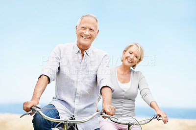 Buy stock photo Happy, portrait and senior couple on bicycle outdoor on vacation, getaway or weekend trip together. Smile, blue sky and elderly man with woman on bike for cycling, bonding or adventure on holiday.
