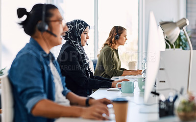 Buy stock photo Shot of a group of young call centre agents wearing headsets and working on their computers in an office