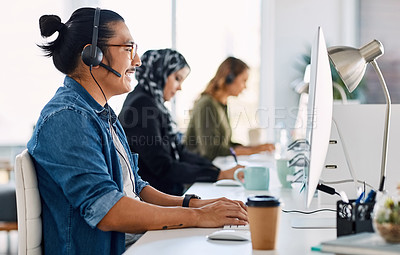 Buy stock photo Shot of a group of young call centre agents wearing headsets and working on their computers in an office