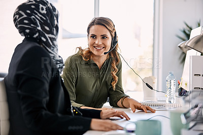 Buy stock photo Shot of two young female call centre agents having a discussion at their work station