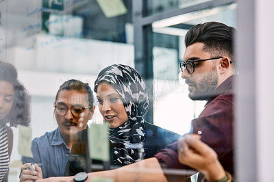 Buy stock photo Shot of a group of young businesspeople planning and writing notes on a glass wall in an office at work