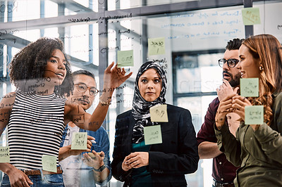 Buy stock photo Shot of a group of young businesspeople planning and writing notes on a glass wall in an office at work