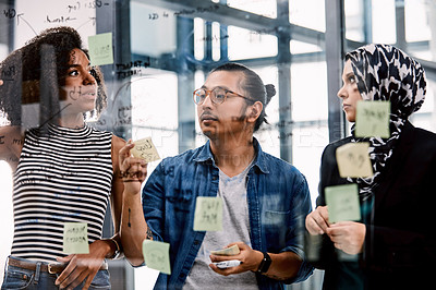 Buy stock photo Shot of a group of young businesspeople planning and writing notes on a glass wall in an office at work