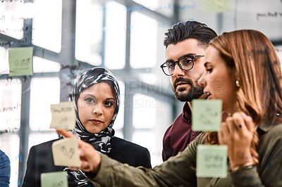 Buy stock photo Shot of a group of young businesspeople planning and writing notes on a glass wall in an office at work