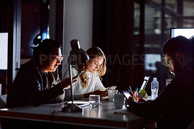 Buy stock photo Shot of a group of young businesspeople using smart devices during a late night meeting at work