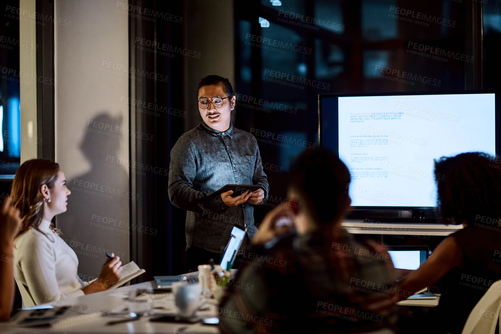 Buy stock photo Shot of a young businessman delivering a presentation during a late night meeting at work