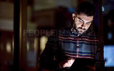 Buy stock photo Shot of a young businessman using a digital tablet during a late night at work