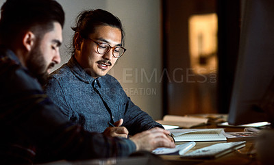 Buy stock photo Shot of two young businessmen going over paperwork together during a late night at work