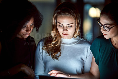 Buy stock photo Shot of a group of young businesswomen using a digital tablet during a late night at work