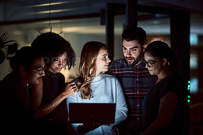 Buy stock photo Shot of a group of young businesspeople using a digital tablet during a late night at work