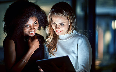 Buy stock photo Shot of two young businesswomen using a digital tablet during a late night at work