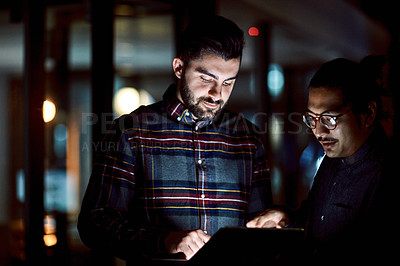 Buy stock photo Shot of two young businessmen using a digital tablet during a late night at work