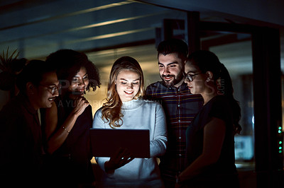 Buy stock photo Shot of a group of young businesspeople using a digital tablet during a late night at work