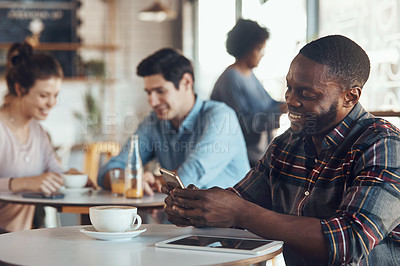 Buy stock photo Shot of a handsome young man sitting in a busy coffee shop while using his cellphone during the day