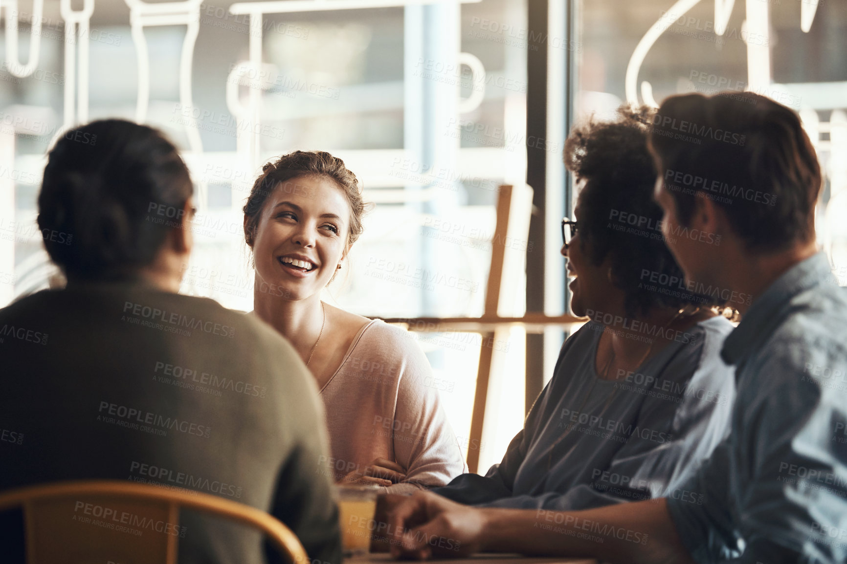 Buy stock photo Shot of a happy young group sitting together and smiling in a coffee shop during the day