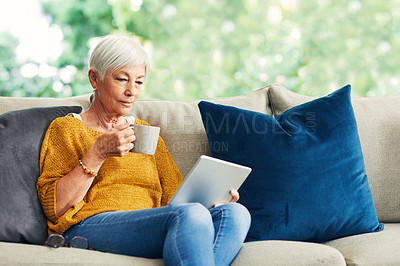 Buy stock photo Shot of a senior woman using a digital tablet and having coffee on the sofa at home