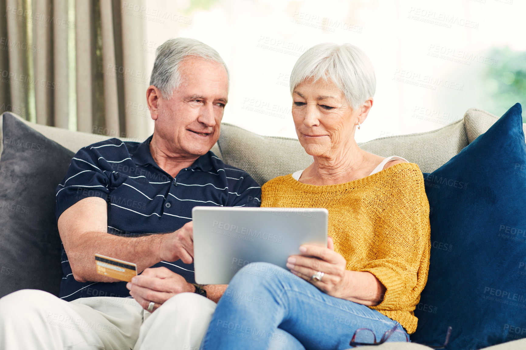 Buy stock photo Shot of a senior couple using a credit card and digital tablet on the sofa at home