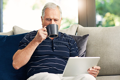 Buy stock photo Shot of a senior man using a digital tablet and having coffee on the sofa at home